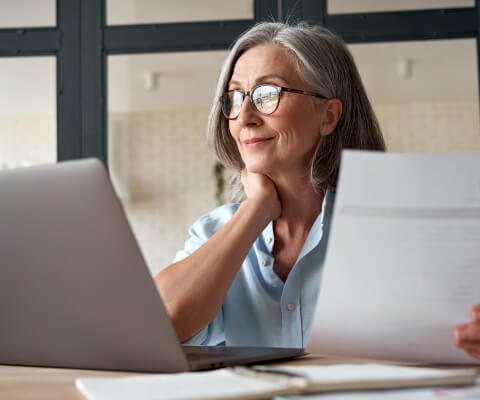 Mature woman holding a document and looking at a laptop