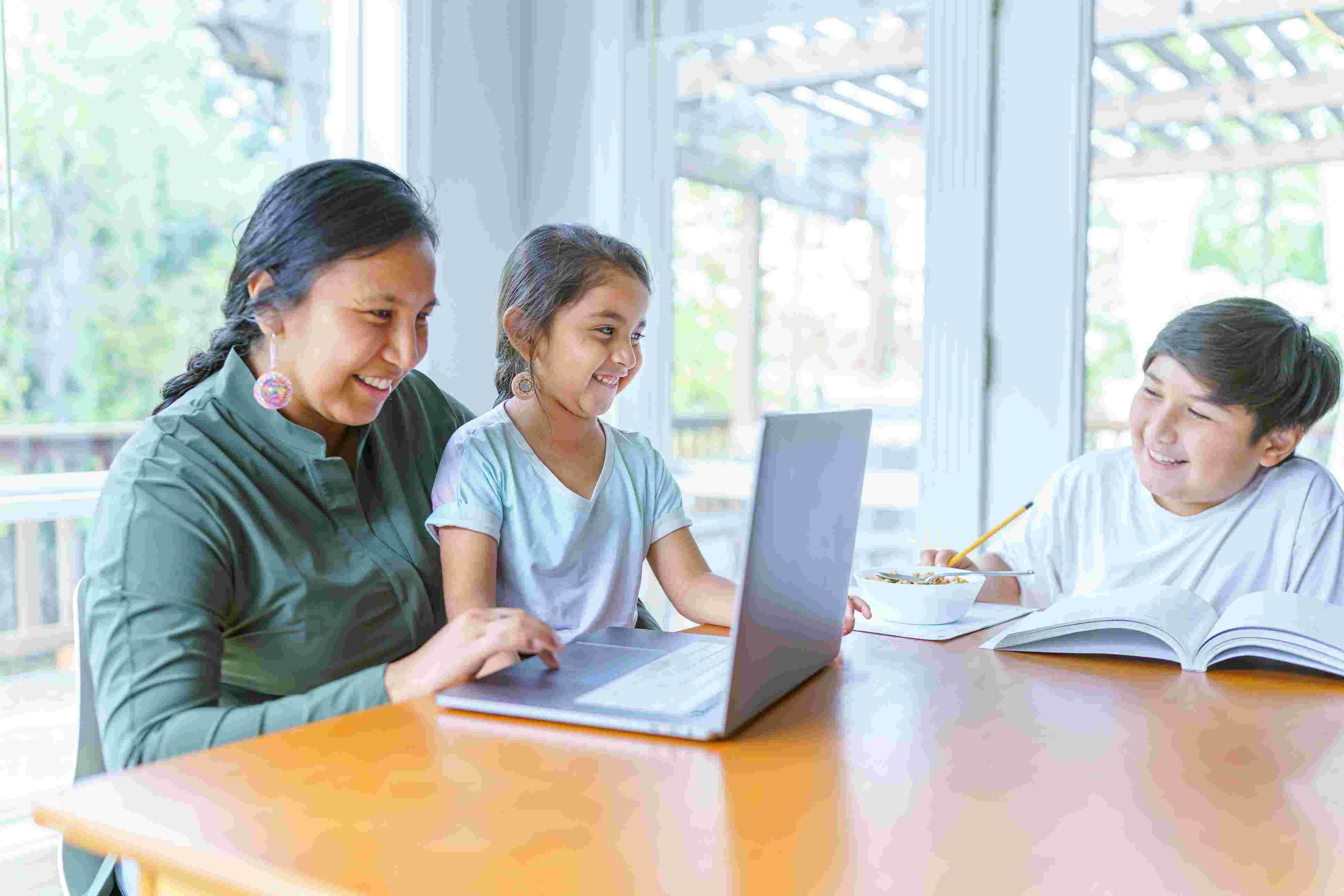 Native woman and her daughter and son at table with laptop